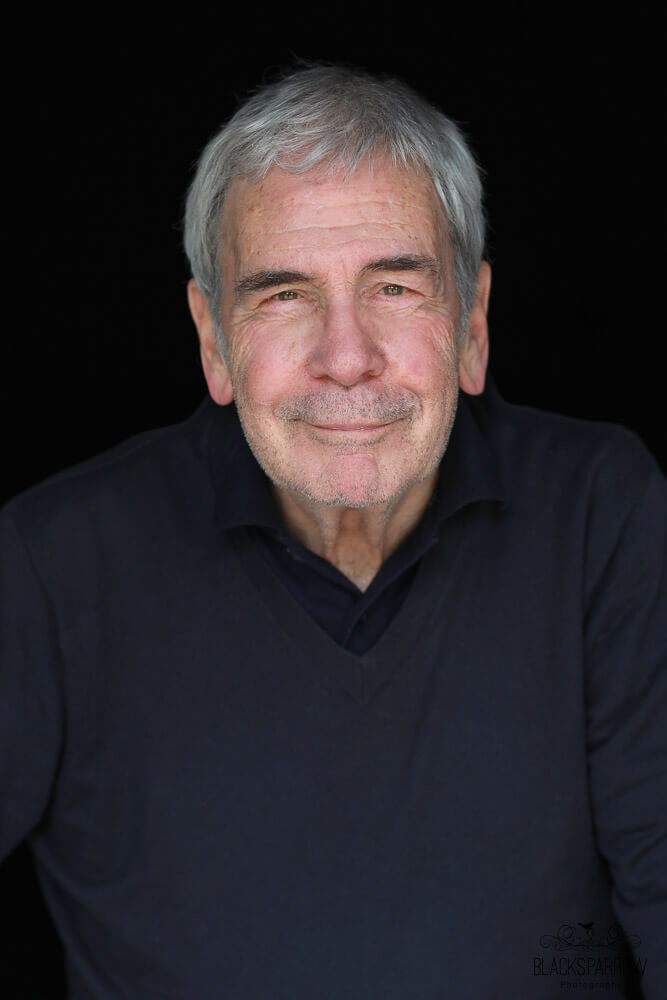 Porträt eines Mannes mit grauen Haaren, der freundlich in die Kamera lächelt.